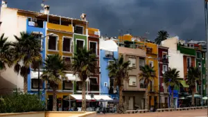 Edificios coloridos con palmeras bajo un cielo gris de tormenta en la costa española.