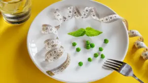 Plato blanco con guisantes, albahaca y cinta métrica sobre fondo amarillo brillante.