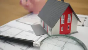 Maqueta de una casa pequeña con una lupa sobre plano inmobiliario