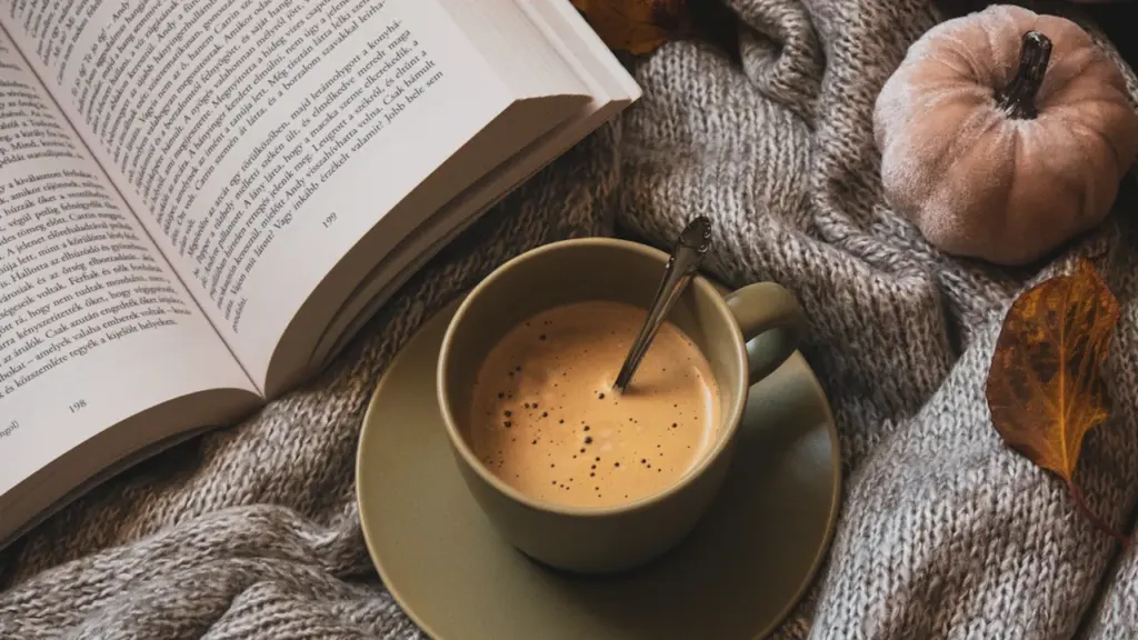 Libro abierto con una taza de café y una manta acogedora en otoño.