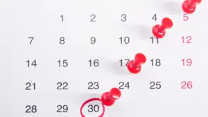 Calendario de pared con fechas marcadas con chinchetas rojas para organizar tareas importantes.