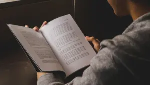 Una persona sosteniendo y leyendo un libro abierto en un entorno tranquilo y acogedor.