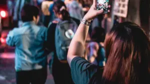 Persona tomando fotografías con su teléfono móvil en un entorno urbano con gente alrededor.