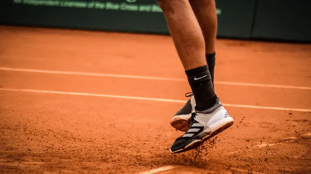 Primer plano de los pies de un tenista saltando sobre una pista de arcilla.