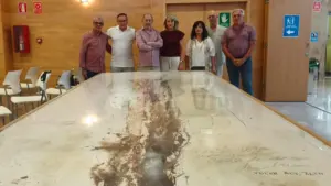 Grupo de siete personas posando detrás de una gran mesa con una obra artística.
