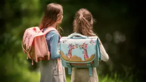 Dos niñas de espaldas con mochilas escolares de diseño ergonómico en un entorno natural.