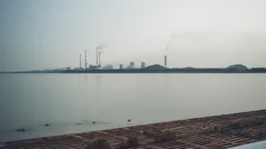 Complejo industrial con chimeneas junto a la costa bajo un cielo nublado.