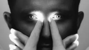 Primer plano de una persona cuyos ojos brillan intensamente mientras sus dedos tocan su rostro.