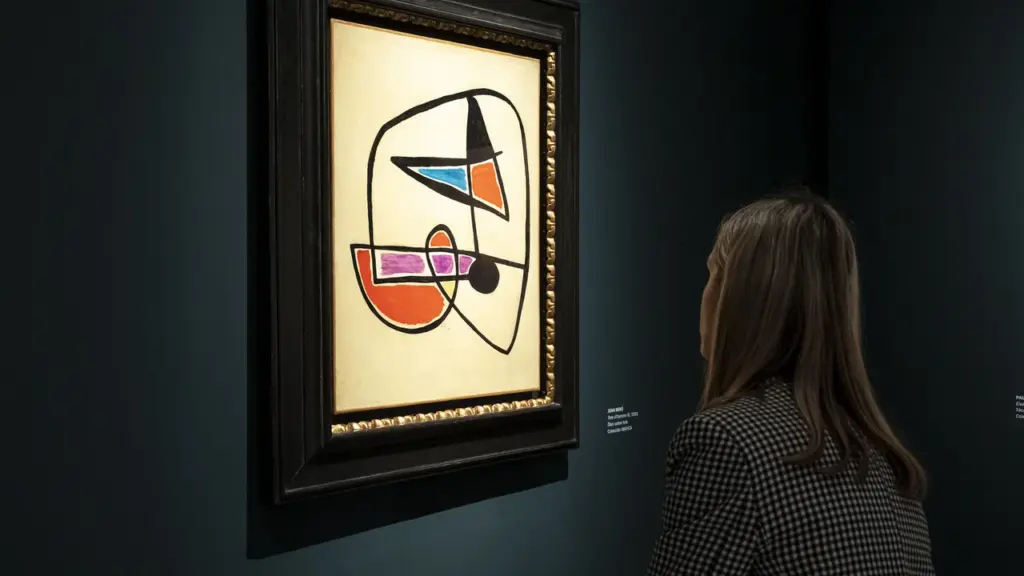 Una mujer observa una pintura abstracta de Joan Miró en un museo con fondo oscuro.