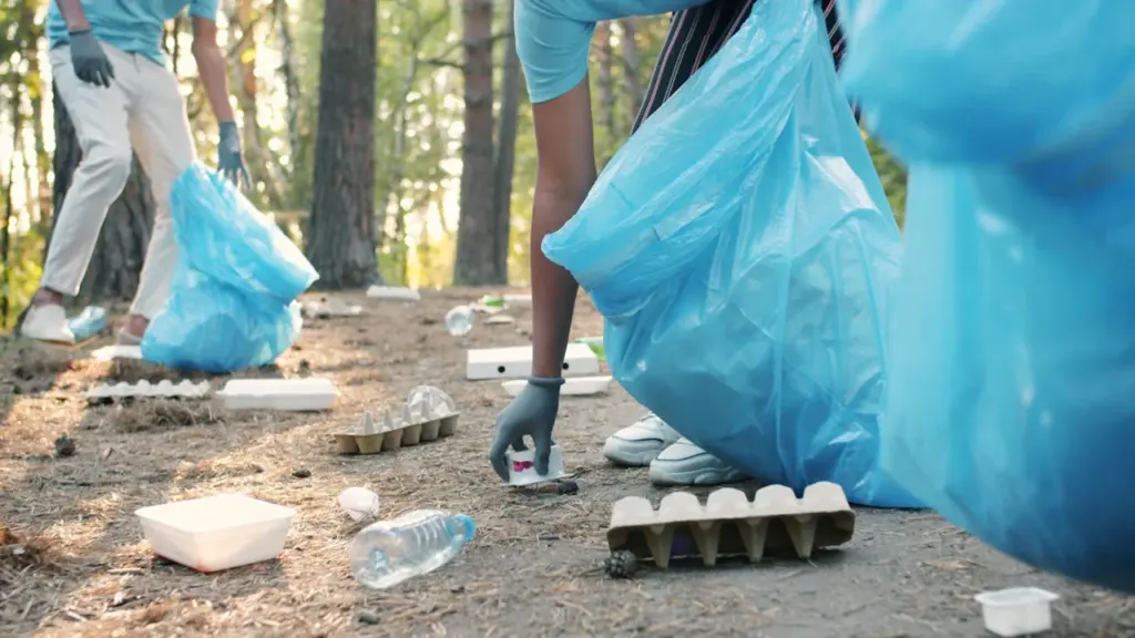 Voluntarios con guantes recogiendo basura en bolsas azules dentro de un entorno forestal natural.