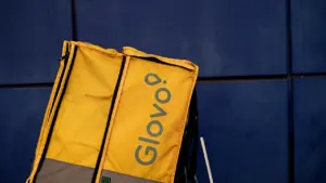 Mochila de reparto amarilla de Glovo contra una pared de metal azul oscuro.