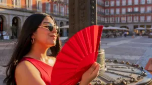 Una mujer con abanico rojo pasea por una plaza céntrica en España.