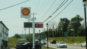Cartel de gasolinera mostrando precios de combustible y coches circulando por la carretera.
