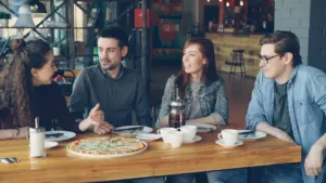 Grupo de amigos conversando atentamente mientras comparten una pizza en un café moderno.