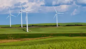 Tres grandes aerogeneradores blancos en un campo verde bajo un cielo azul con nubes.