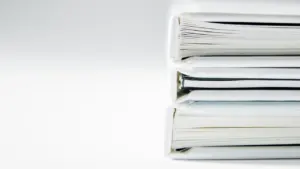 Pilas de carpetas y documentación administrativa sobre una superficie blanca y limpia.