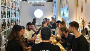 Grupo de personas cenando y bebiendo cerveza en un bar con estanterías llenas de botellas.
